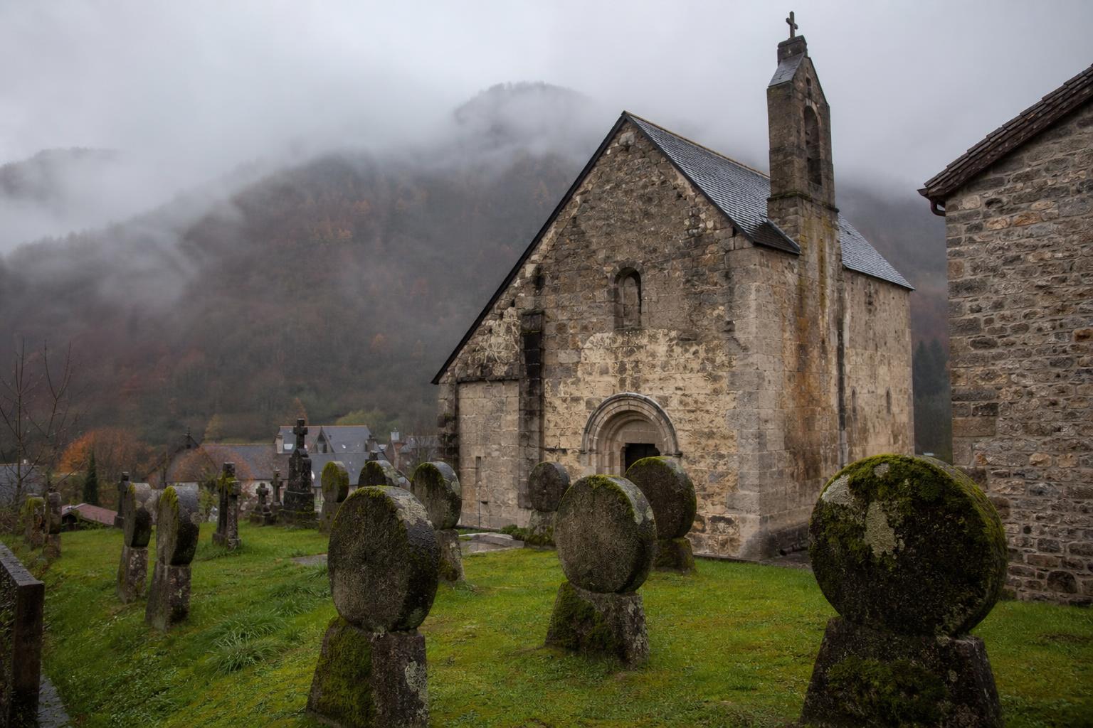 Église romane Santa Grazi du XIe siècle à Sainte-Engrâce, cimetière avec stèles discoïdales couvertes de mousse, brume en arrière-plan