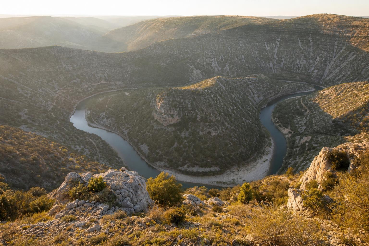Vue plongeante sur le cirque de Navacelles depuis le belvédère de Blandas, méandre de la Vis autour de l'éperon rocheux, lumière de fin d'après-midi, causse aride