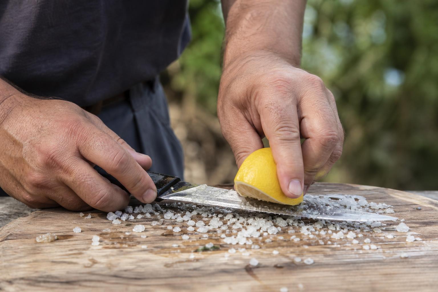 Mains frottant un couteau de pêche avec du citron et du gros sel sur un plan de travail extérieur