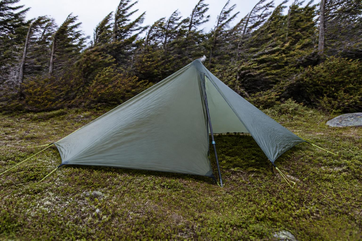 Tarp monté en configuration demi-pyramide : un bâton au centre, trois coins plaqués au sol, un côté ouvert