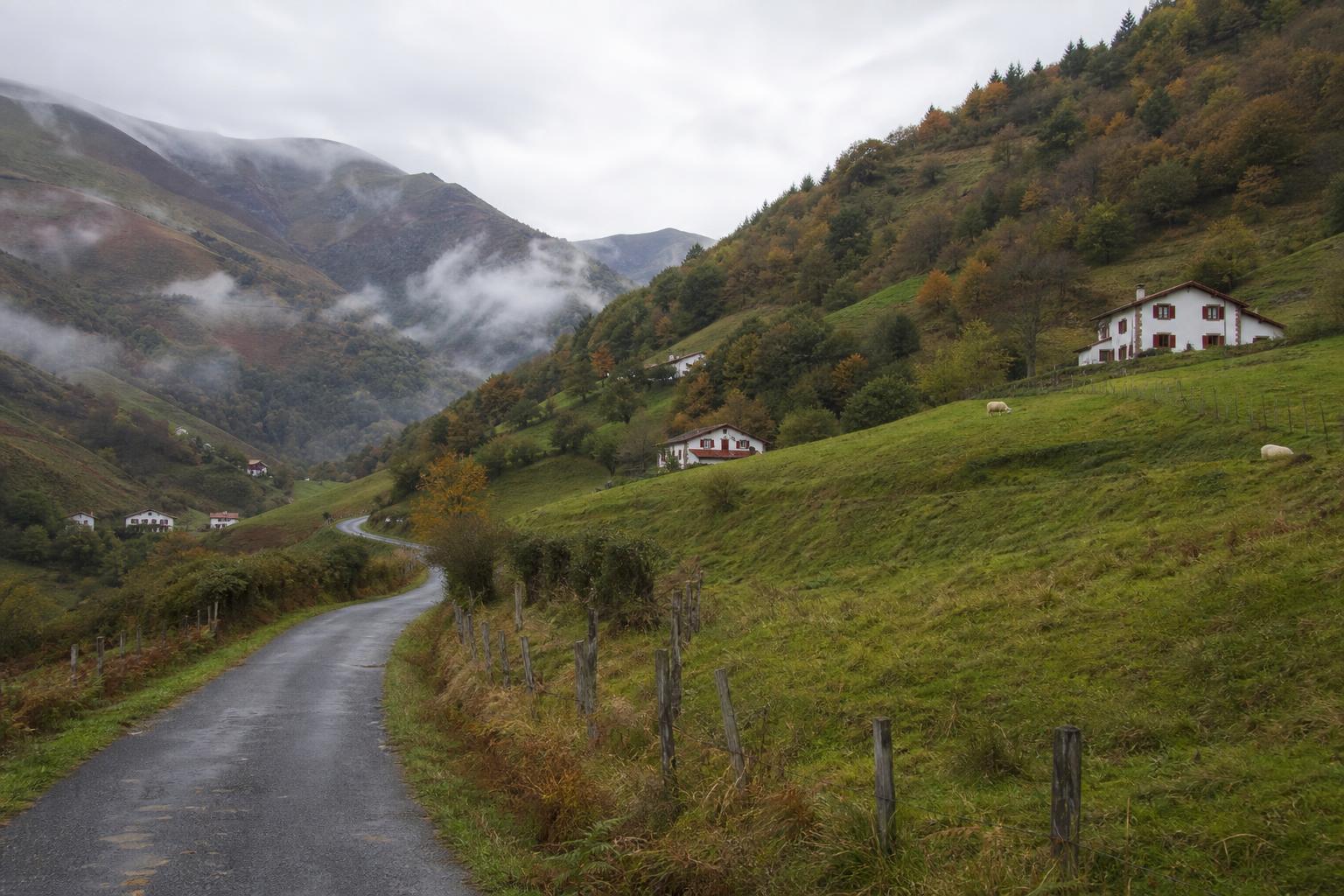 Vallée étroite des Aldudes en automne, maisons blanches aux volets rouges dispersées sur les pentes verdoyantes, brume matinale dans le lointain