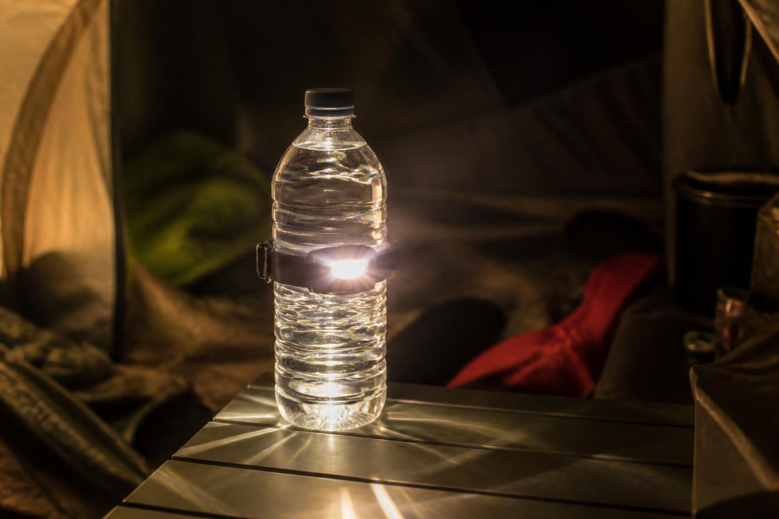 Lampe frontale fixée autour d'une bouteille d'eau transparente, la lumière se diffuse à travers l'eau dans la pénombre