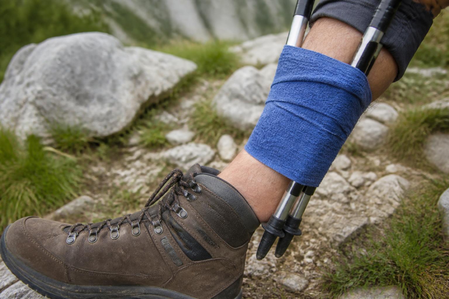 Attelle improvisée avec deux bâtons de randonnée strappés autour d'une jambe, sur un sentier rocailleux