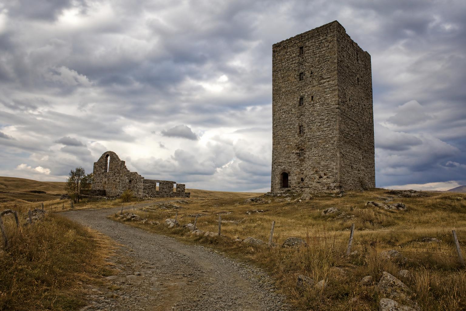 Vestiges de la Dômerie d'Aubrac et la Tour des Anglais sous un ciel d'automne chargé, pâtures désertes alentour